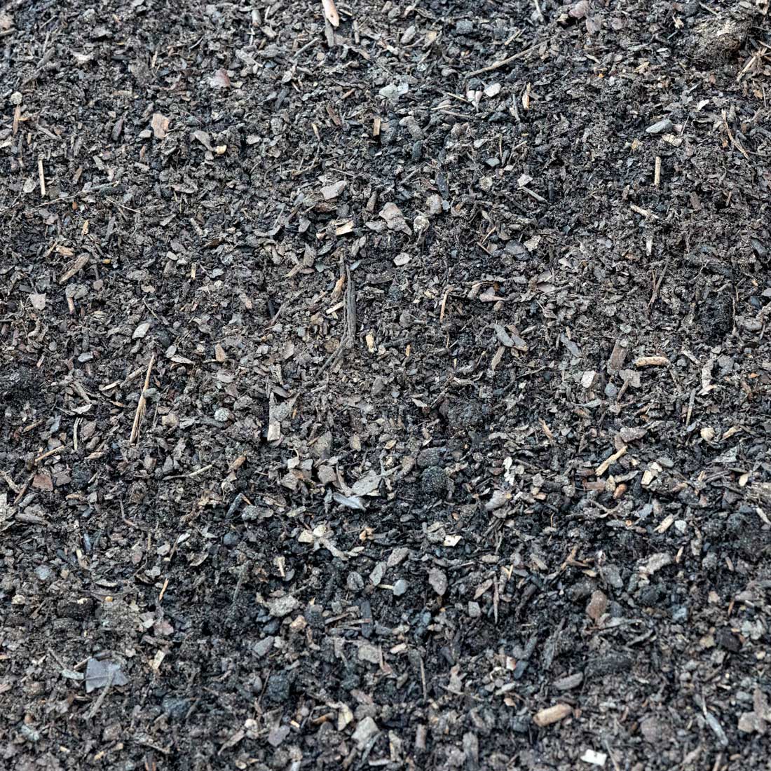 A close-up texture shot of dark, rich compost or soil mix containing shredded leaves, wood chips, and organic matter.
