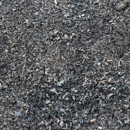 A close-up texture shot of dark, rich compost or soil mix containing shredded leaves, wood chips, and organic matter.
