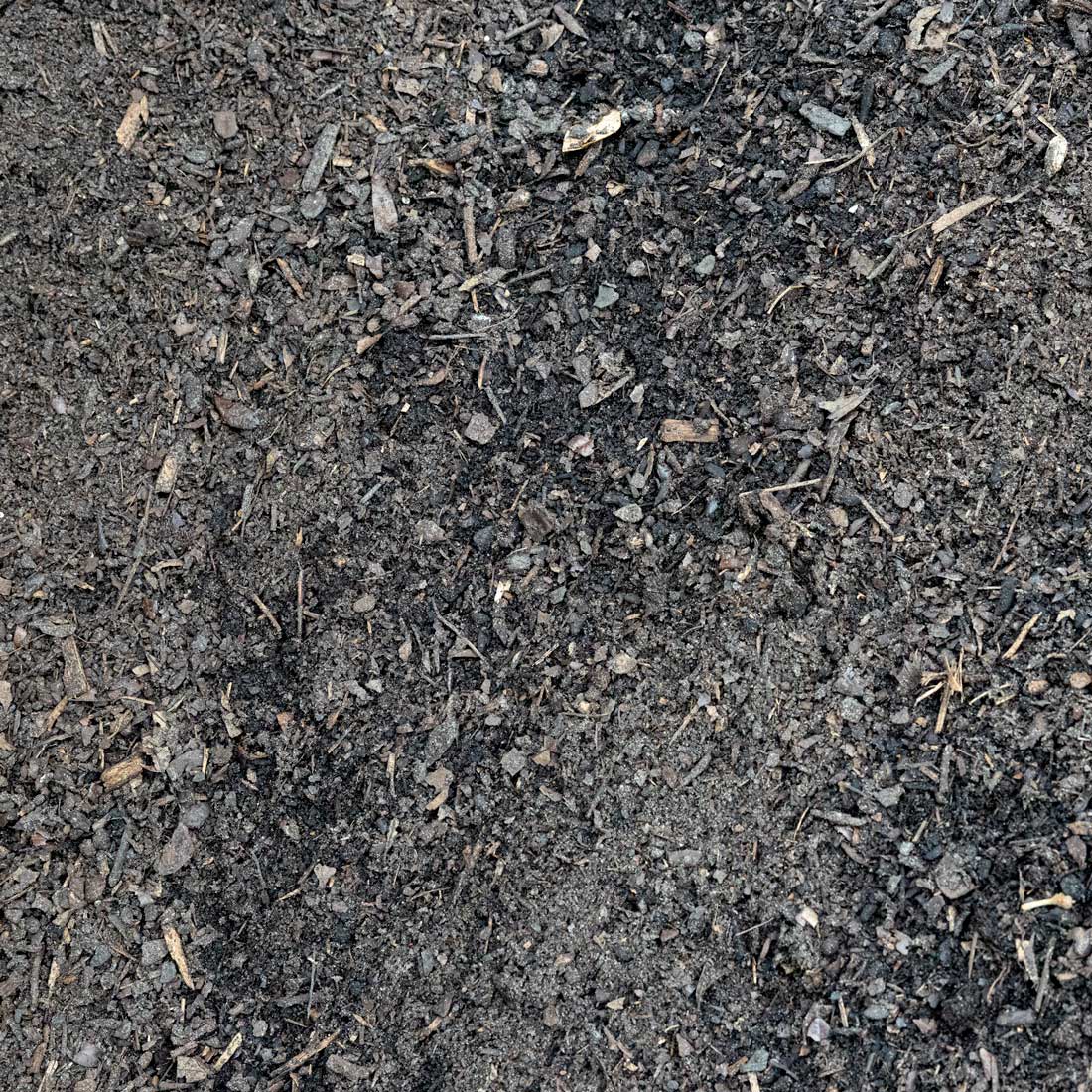 A close-up texture shot of dark, granular compost or soil with visible wood chips and organic debris.