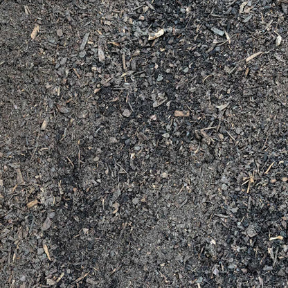 A close-up texture shot of dark, granular compost or soil with visible wood chips and organic debris.