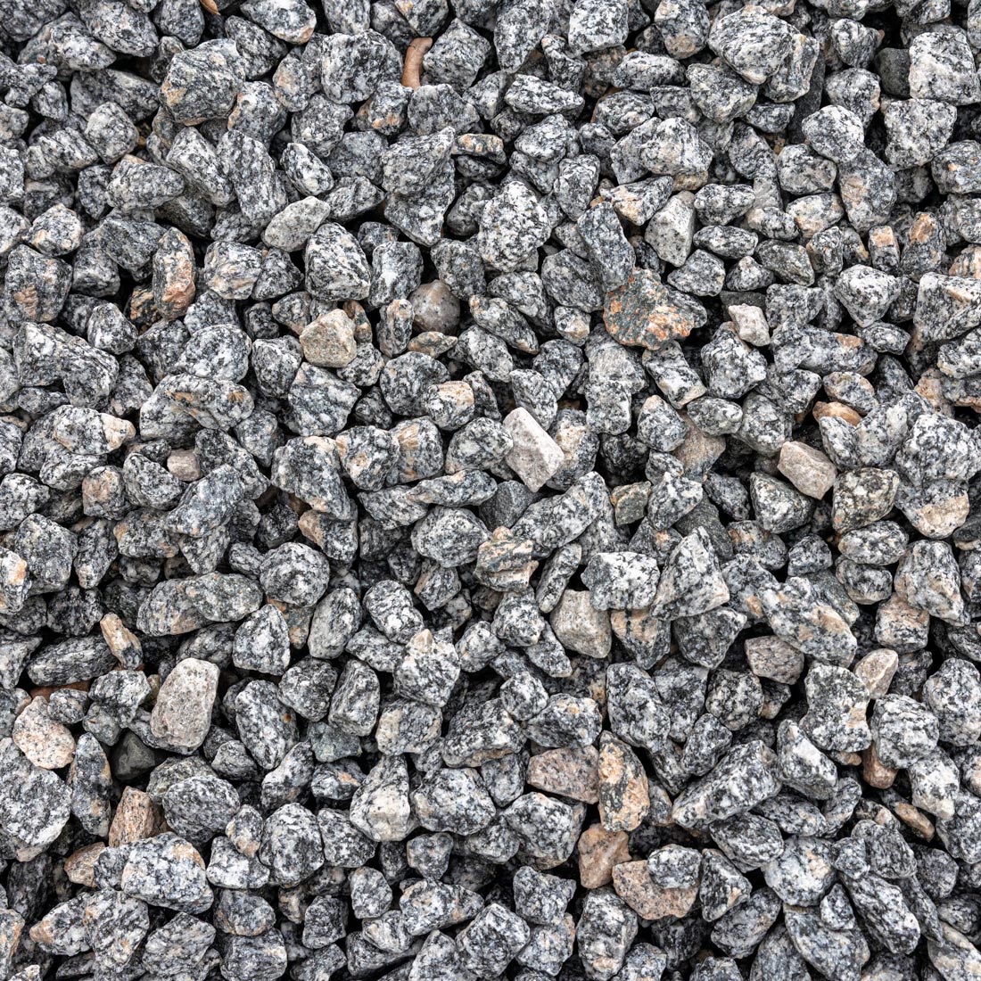 A close-up, top-down view of small gray and black granite river rocks or gravel chips with some lighter beige and brown stones mixed in, filling the entire frame.