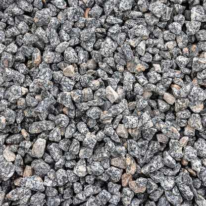 A close-up, top-down view of small gray and black granite river rocks or gravel chips with some lighter beige and brown stones mixed in, filling the entire frame.