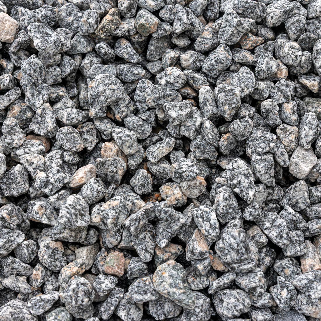 A close-up, top-down view of crushed stone gravel with a speckled gray, black, and white granite texture, with a few small tan and reddish-brown stones mixed in.