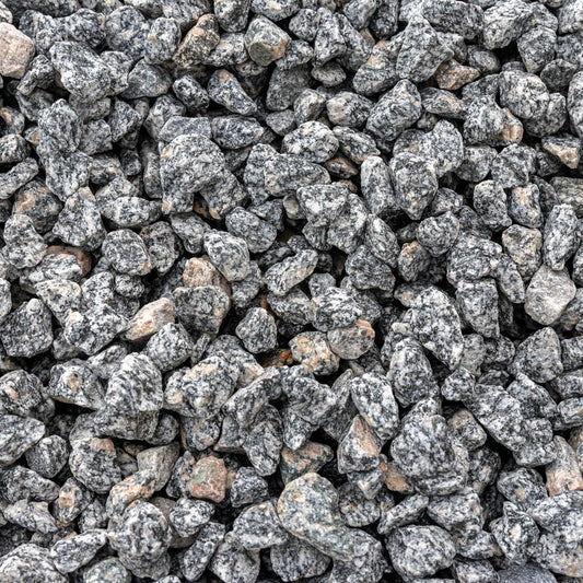 A close-up, top-down view of crushed stone gravel with a speckled gray, black, and white granite texture, with a few small tan and reddish-brown stones mixed in.