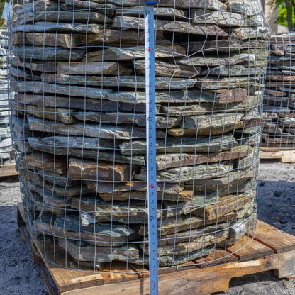 Stack of stone slabs in a wire mesh on a wooden pallet with a measuring tape for scale.